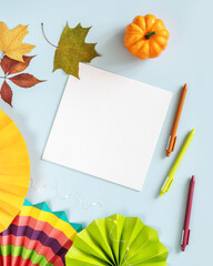 Autumn composition with white sheet of paper, colorful paper fans, pens and decorations on a blue...