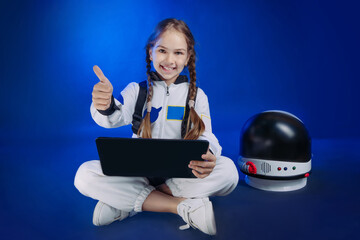 Teenager girl wearing astronaut costume using laptop sitting on dark blue background