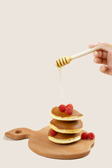 A woman pours honey on a stack of pancakes with raspberries