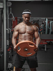 Fototapeta na wymiar Muscular athletic african american guy exercising with weight plate in gym. Strength workout concept