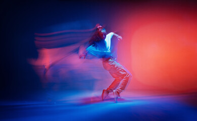 Dancing female standing on tiptoe in colourful neon studio light. Long exposure. Contemporary hip hop dance - obrazy, fototapety, plakaty
