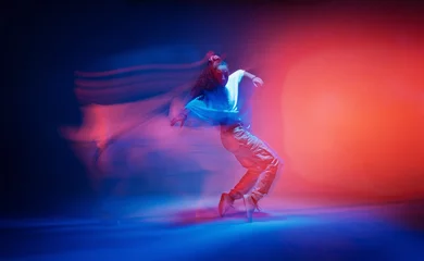 Gordijnen Dancing female standing on tiptoe in colourful neon studio light. Long exposure. Contemporary hip hop dance © Georgii