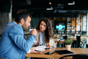 Young businesswoman talks to male colleague while having meeting at cafe.
