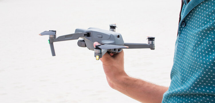 A man's hand is holding a flying drone or quadcopter. Flying over the ground. Video and photo shooting technologies.