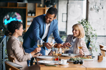 Young happy businessman serves food to his colleagues during lunch in restaurant.