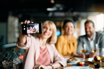 Close-up of co-workers take selfie during business lunch in restaurant.