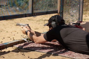 Man in tactical clothes shooting from a pistol, reloading the gun and aiming at the target in the open-door Shooting range