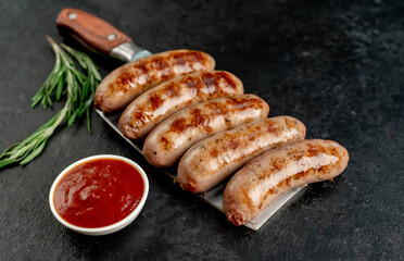 grilled sausages, on a meat knife on a stone background