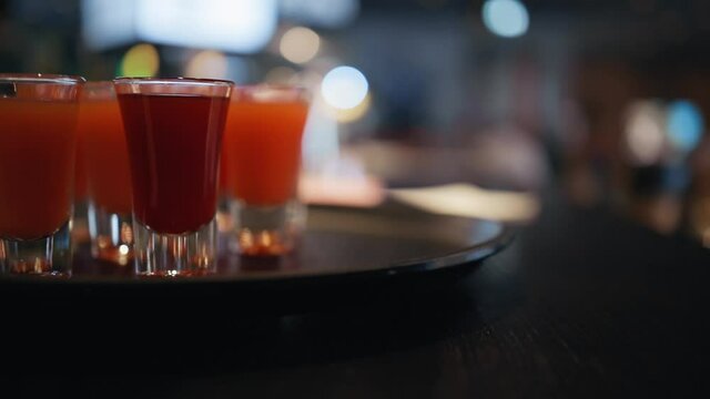 Pan up: Red or orange shots at bar counter in pub with blue blinking light in blurry background