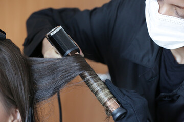 Fixing a woman's beautiful, blonde hair with a black curling iron.