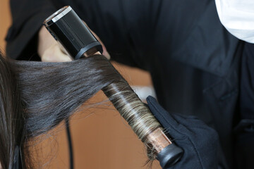 Fixing a woman's beautiful, blonde hair with a black curling iron.