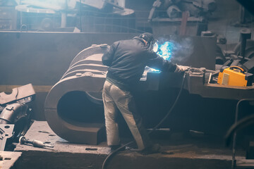 Welder processes large cast iron part in metallurgical plant after it has been melted or...
