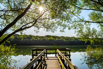 Ruislip Lido wooden viewing platform over the water with Ruislip woods in the distance on a sunny day with sunburst. Ruislip Lido, Ruislip, UK