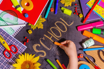 Children's hand writes the word "school" on a black chalkboard