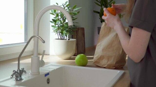Food online delivery. woman washes groceries from store. Take fruit out of paper bag by kitchen sink. Healthy vegetarian breakfast. Delicious vitamins. purity of products. Happy woman fruit at kitchen