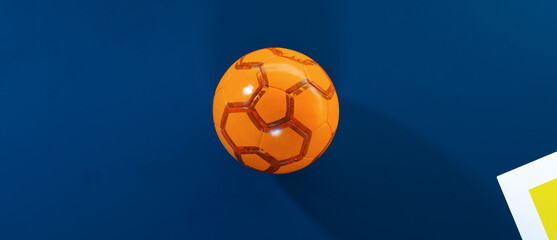 Centered orange futsal indoor soccer ball on a blue field with shadow background