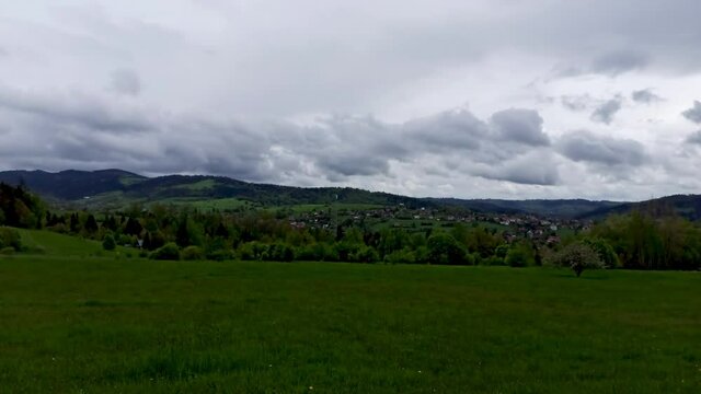 Pan shot of beautiful landscape showing panorama view of green meadow countryside field with single tree in the center against dramatic clouds during rain near Rabka located in Poland, Europe