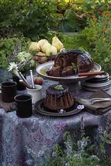 A table set for tea in the garden on a summer evening. On the table is a chocolate muffin and ceramic cups.