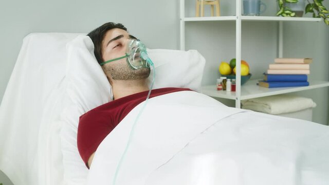 Sick Patient Lying With Oxygen Mask In Hospital Ward, Serious Bad Human Condition With Coronavirus. Suffering Covid Man With Oral-nasal Mask And Oxygen Flow. Anesthesia Face Mask, Breathing Gas.