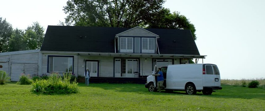 HANDHELD WIDE Adult Mature Caucasian female signing documents with handyman general worker in front of her house. White car with copy space. Shot with 2x anamorphic lens