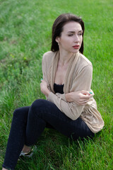 beautiful brunette woman sitting on green grass.