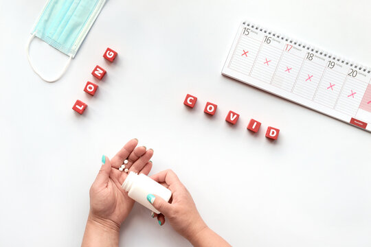 Text Long Covid On Red Cubes. Hand With Pills. Text Long Covid, Patient Hands With Pills. German Text On Weekly Planner Means Days Of The Week. Cancellation, Change Of Plans. Chronic Covid Illness