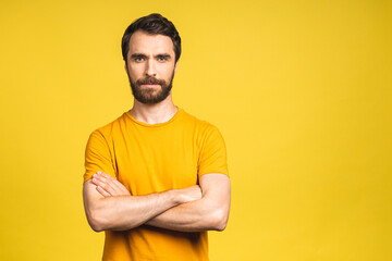 Portrait of serious fashionable handsome man in casual holding crossing hands and looking at camera isolated over yellow background.