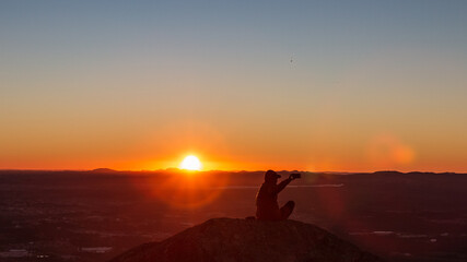 Obraz na płótnie Canvas Pessoa curtindo o pôr do Sol no alto de uma montanha.