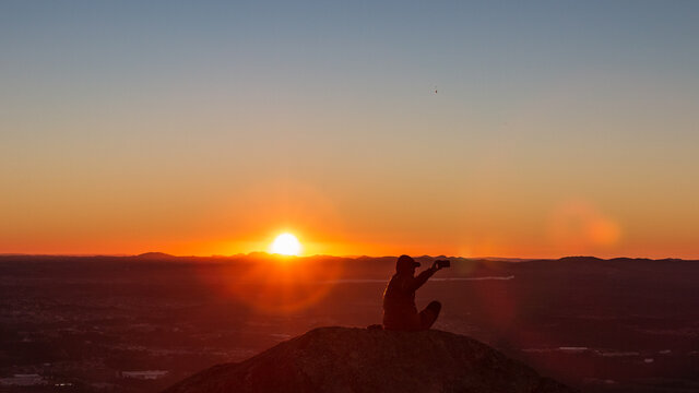 Pessoa curtindo o p&ocirc;r do Sol no alto de uma montanha.