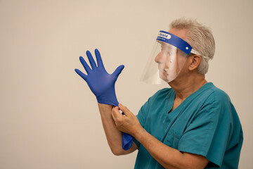 Doctor or nurse wearing a face shield mask and putting on blue latex gloves