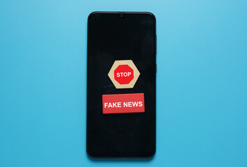 A picture of stop sign on hexagon wood cut and fake news at red wood on smartphone. Fake new caused...