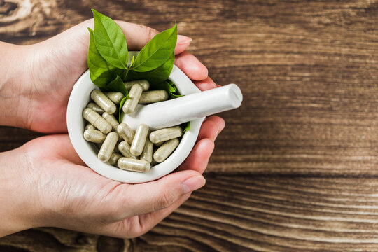 Close-up view of hands holding Andrographis paniculata( Kariyat )capsules with green leaf in mortar on wooden background, Thailand herbal therapy, Alternative medicinal herb treatment concept.