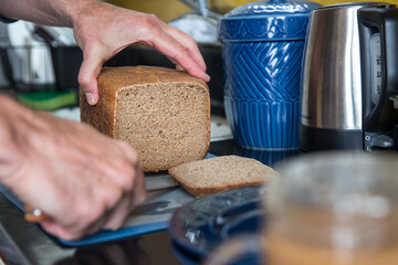Homemade rye bread is sliced by a knife on a cutting board. 