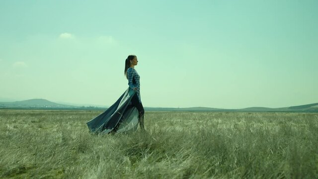 Side view of Woman walking in slow motion through a field . Young stylish lonely woman walking on meadow field . Long skirt fabric flowing by wind . Fashion style . Shot on ARRI Alexa Cinema Camera