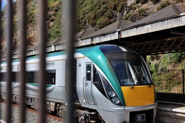 A silver, green, yellow train with a diesel locomotive standing at a railway station.