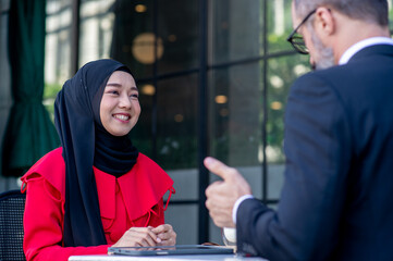 businessman caucasian and businesswoman Muslim working outdoor in the front of a coffee shop.