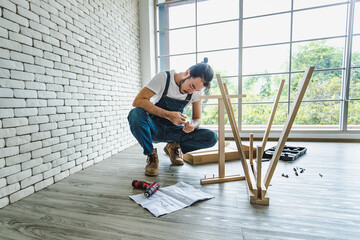 Hipster young man working as handyman looking to manual during assembling wood table with equipments, concept for home diy and self service.in the office