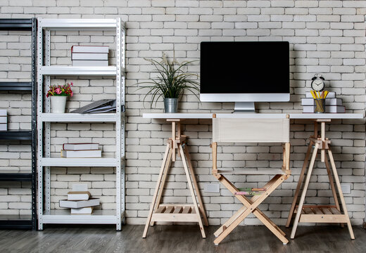 Minimal style with less decorate office coner with metal shelf, computer director chair and wooden table with brick wall background. Concept of work at home