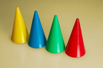 four different colored cone shaped game pieces in a row against ocher yellow background