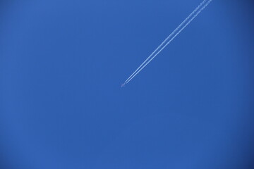 くっきりと飛行機雲を描きながら、飛行機が青空を飛ぶ風景