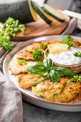 Zucchini pancakes with herbs and sour cream on a plate close-up vertical photo. Vegetarian dish