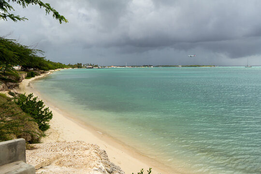 Storm clouds over the beach in Oranjestad, Aruba as a plane lands in the distance. .