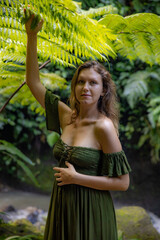 Portrait of beautiful woman under the fern leaves. Caucasian woman wearing green dress walking in tropical rain forest. Nature concept. Travel to Asia. Bali island, Indonesia