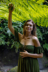 Portrait of beautiful woman under the fern leaves. Caucasian woman wearing green dress walking in tropical jungle. Nature concept. Travel to Asia. Bali island, Indonesia