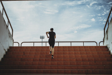 A beautiful woman runner is jogging up the steps under the sunlight. The concept of stepping into success, self-improvement in exercise.