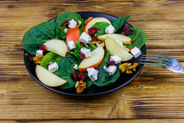 Autumn spinach salad with apple, feta cheese, walnut and dried cranberry on wooden table. Healthy vegetarian food