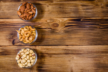 Various nuts (almond, cashew, hazelnut) in glass bowls on a wooden table. Vegetarian meal. Healthy eating concept. Top view