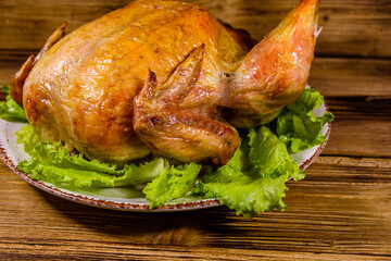 Plate with roasted whole chicken and lettuce leaves on a wooden table
