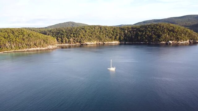 Aerial - wide drone shot of single boat in secluded island bay, Tasmania