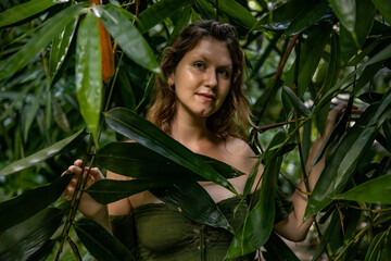 Woman's face surrounded by bamboo leaves. Portrait of beautiful woman in tropical rain forest. Lush green plants in jungle. Nature concept. Bali, Indonesia